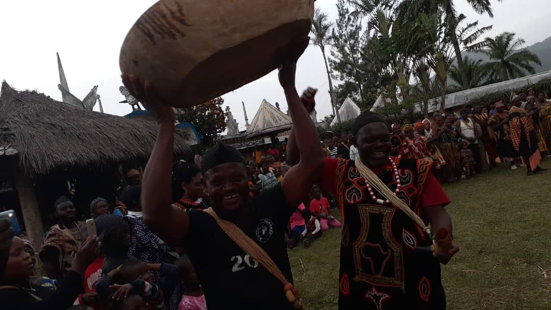 A smiling man raises a large carved wooden bowl above his head beside a man in a Meta gown