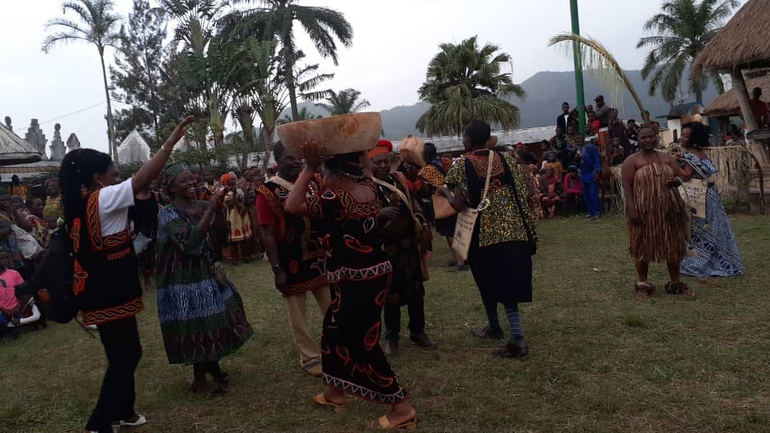 Dancers in Meta dress on the Guneku Palace ground, one carrying a carved wooden bowl on her head