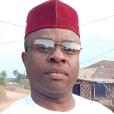 Tayong Fah Elvis, head and shoulders, wearing a red cap and glasses, photographed outdoors in the village.
